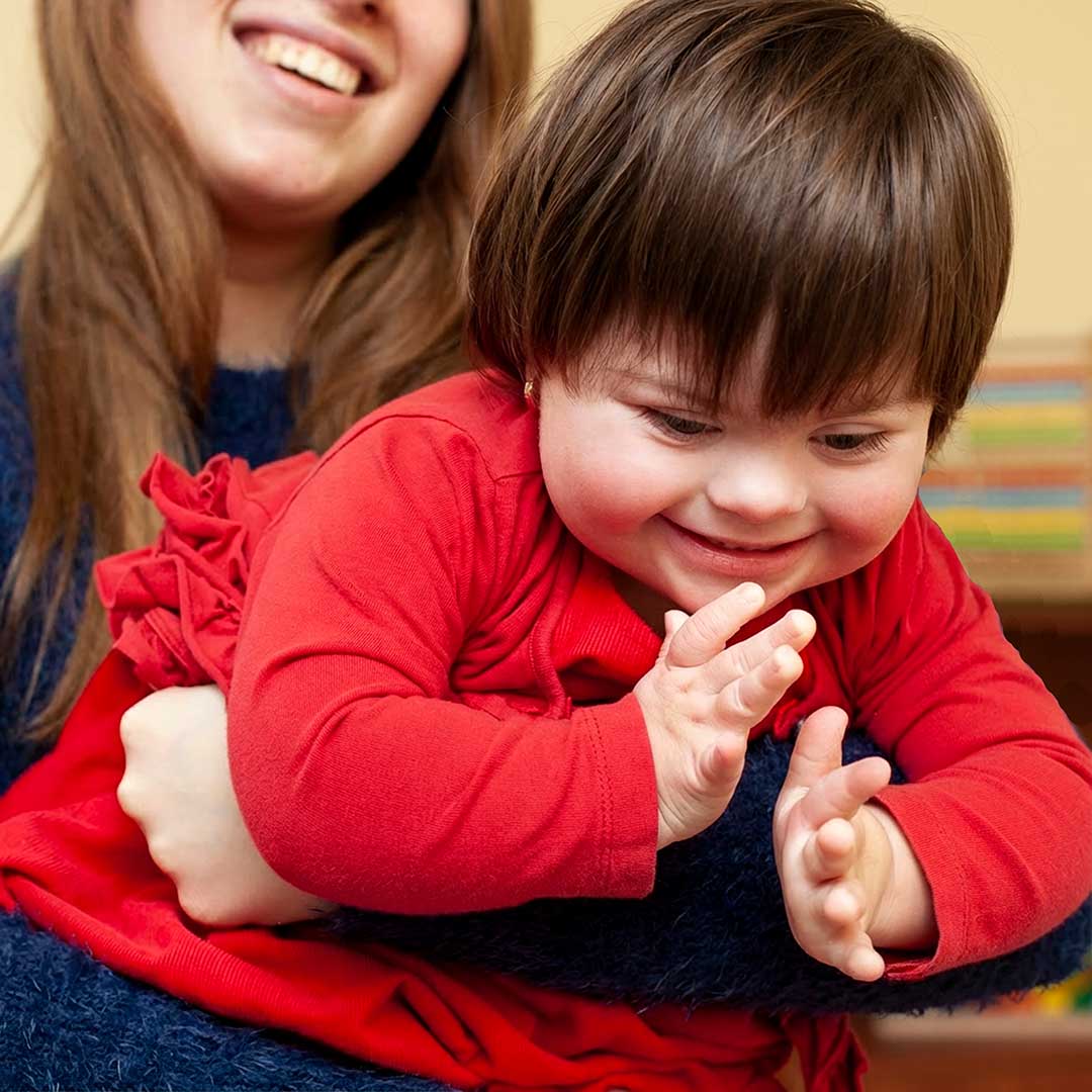 Managing Caregiver Stress for Parents of Children with Disabilities Parent helping a smiling child with down syndrome playing in a living room, representing the daily dedication of family caregivers.